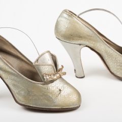 A pair of heeled, metallic shoes. The shoes have a decorative ribbon on the front.